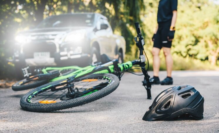 A green bicycle and a black helmet lie on the asphalt after a crash involving a vehicle with bright headlights.