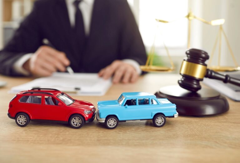 Red and blue toy cars beside a judge’s gavel and scales on a desk.