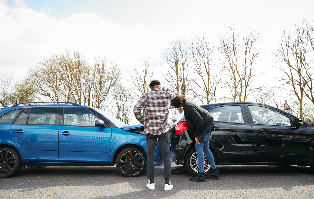 Young male and female drivers inspect rear-end collision damage, highlighting the importance of witness statements after a crash.