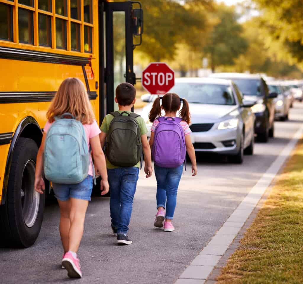 Kids are walking towards school bus and traffic is waiting to pass the school bus
