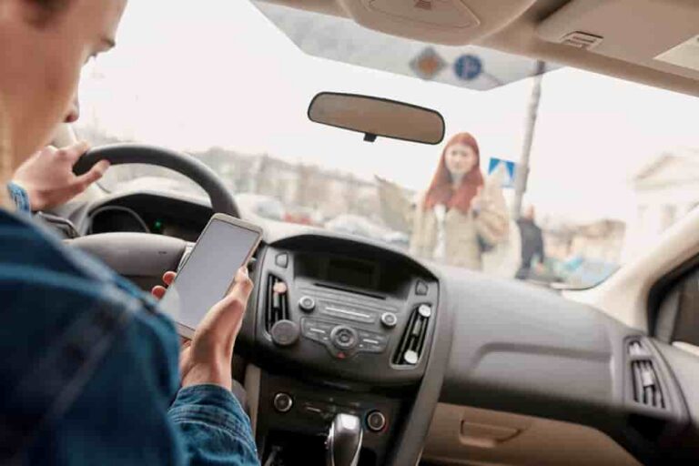Driver holding a mobile phone with a pedestrian visible through the windshield.