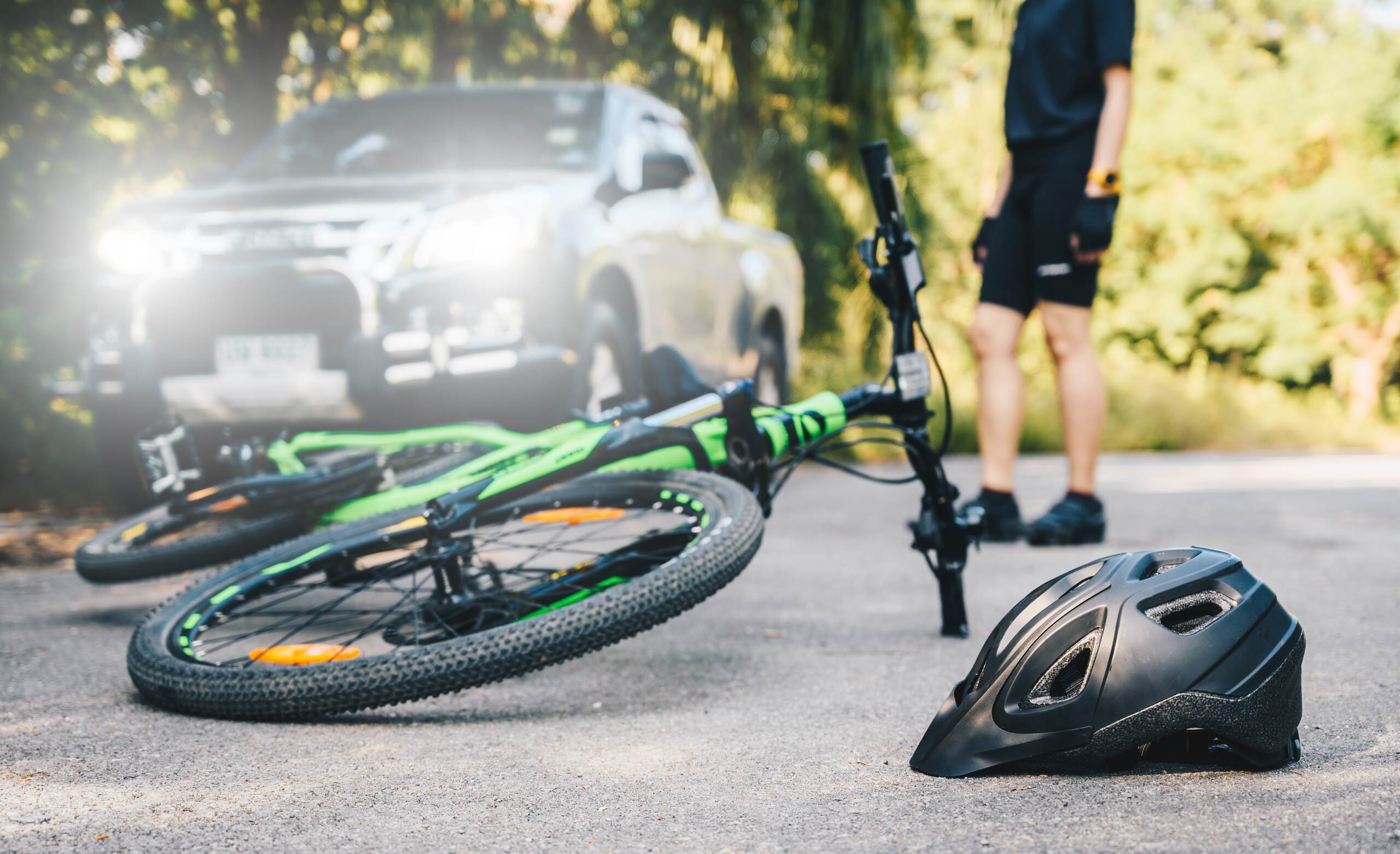 A green bicycle and a black helmet lie on the asphalt after a crash involving a vehicle with bright headlights.