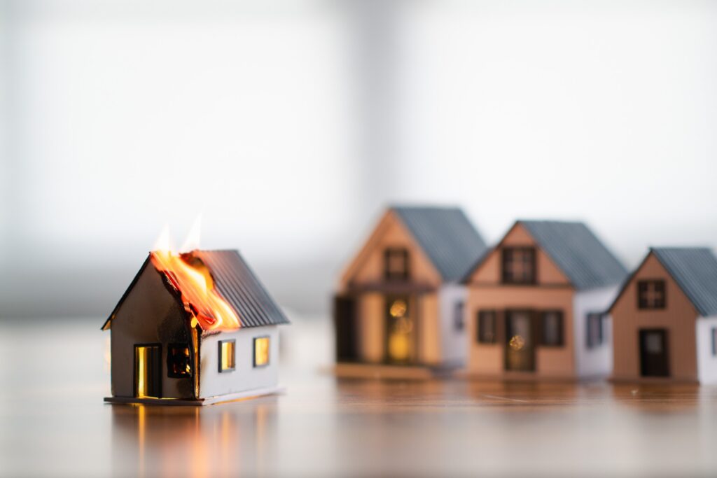 Miniature houses on a tabletop, with flames rising from the roof of one model.