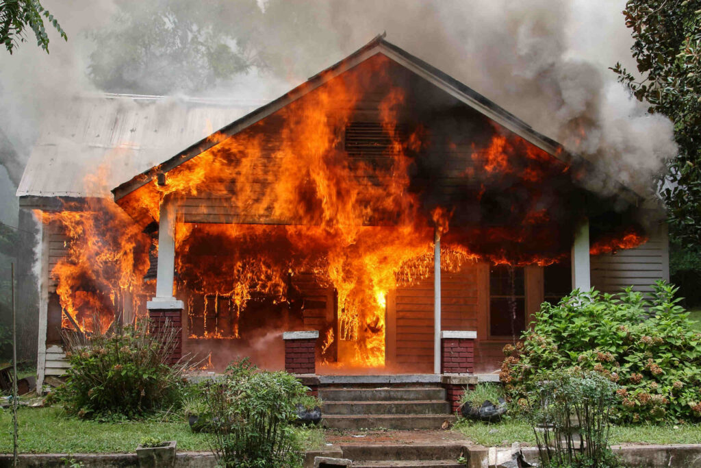 A residential building engulfed in large, intense orange flames and heavy smoke.