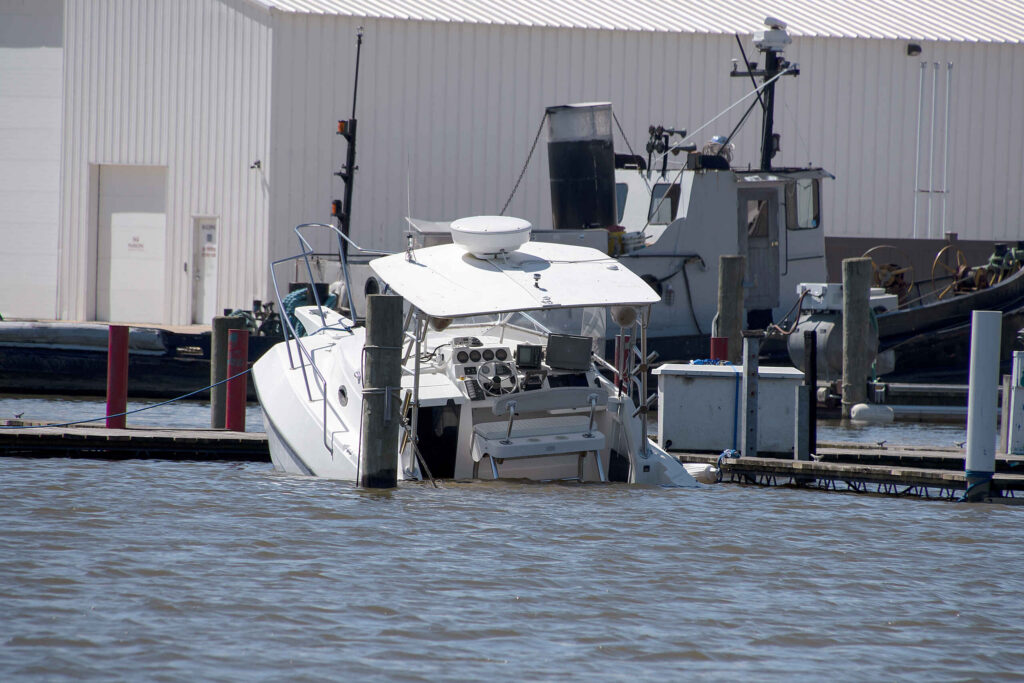 A white motorboat partially submerged and sinking at a dock following an accident.