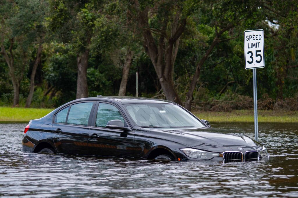 A black sedan partially submerged in deep floodwater next to a 35 MPH speed limit sign along a tree-lined road, showcasing hazardous driving conditions handled by Broward County car accident lawyers.