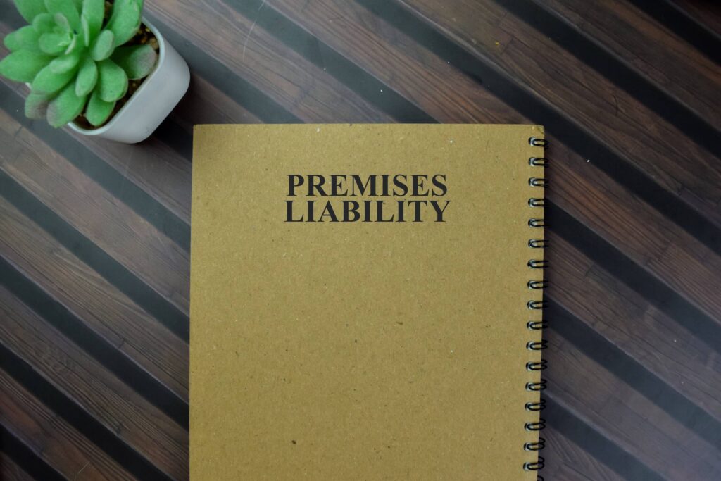A top-down view of a spiral notebook with "Premises Liability" printed on its brown cover, sitting next to a small green potted succulent on a dark wooden table, representing injury claims managed by Broward County premises liability lawyers.