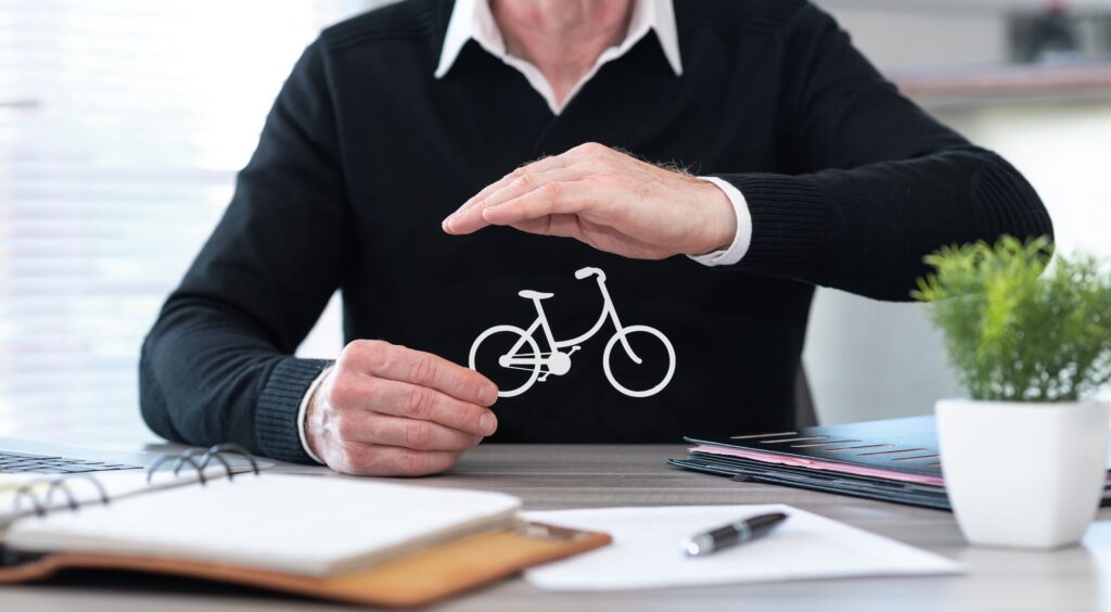 A man at a desk protecting a paper cutout of a bicycle with his hands, symbolizing legal and insurance protection offered by Broward County Bicycle Accident Lawyers.
