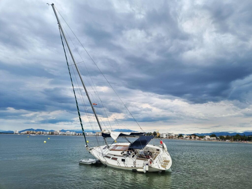 A white sailboat listing heavily to one side in shallow water under a dark, cloudy sky, illustrating property damage claims handled by Broward County Boating Accident Lawyers.