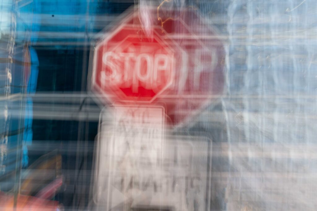 A heavily blurred, double-vision abstract shot of a red stop sign and street signs, visually representing the disorientation and danger associated with a drunk driver in Broward County.