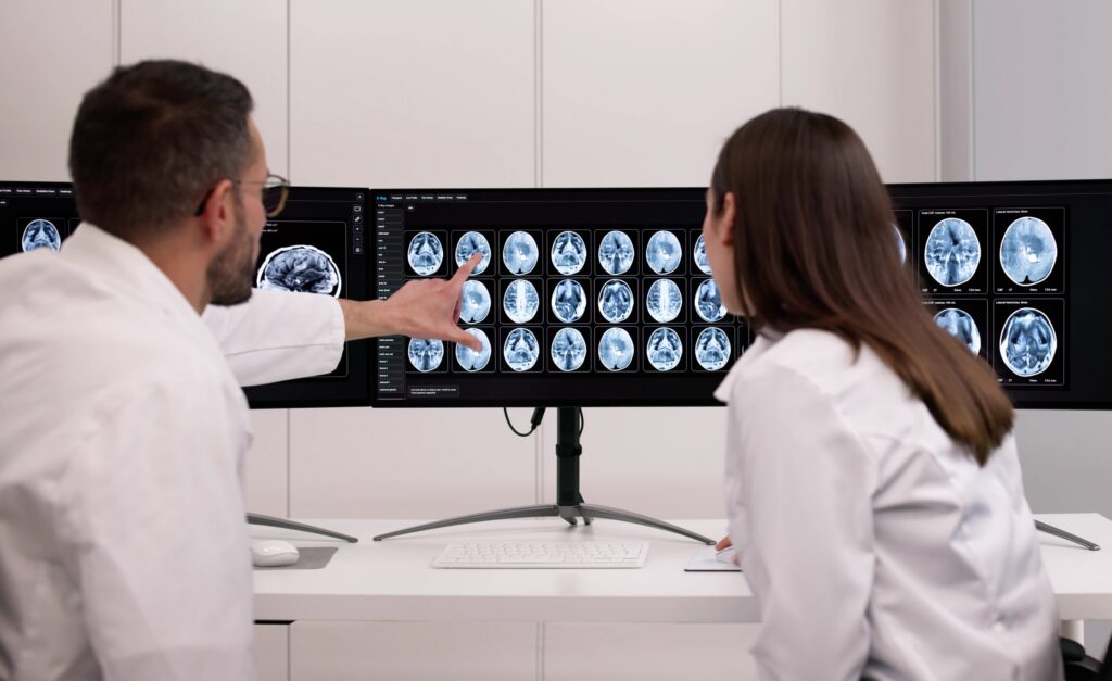 Two medical professionals reviewing multiple brain scan slices on large computer monitors, representing the complex diagnostic reviews handled by Broward County Traumatic Brain Injury Lawyers.