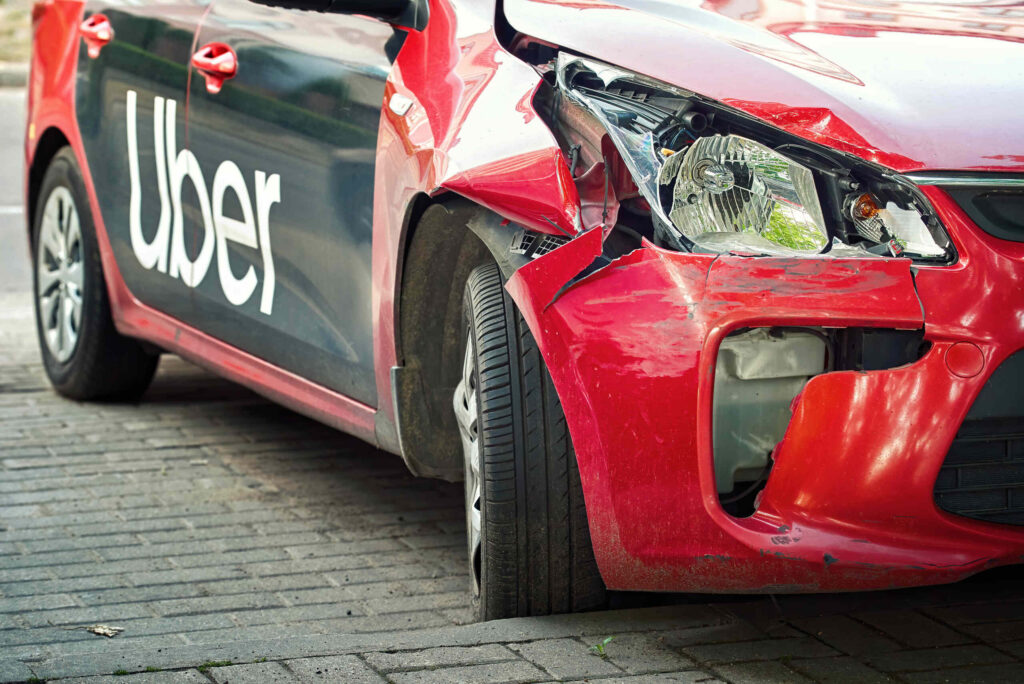Front-end damage to a red car with an Uber logo on the side door, highlighting the need for Broward County Ridesharing Accident Lawyers.