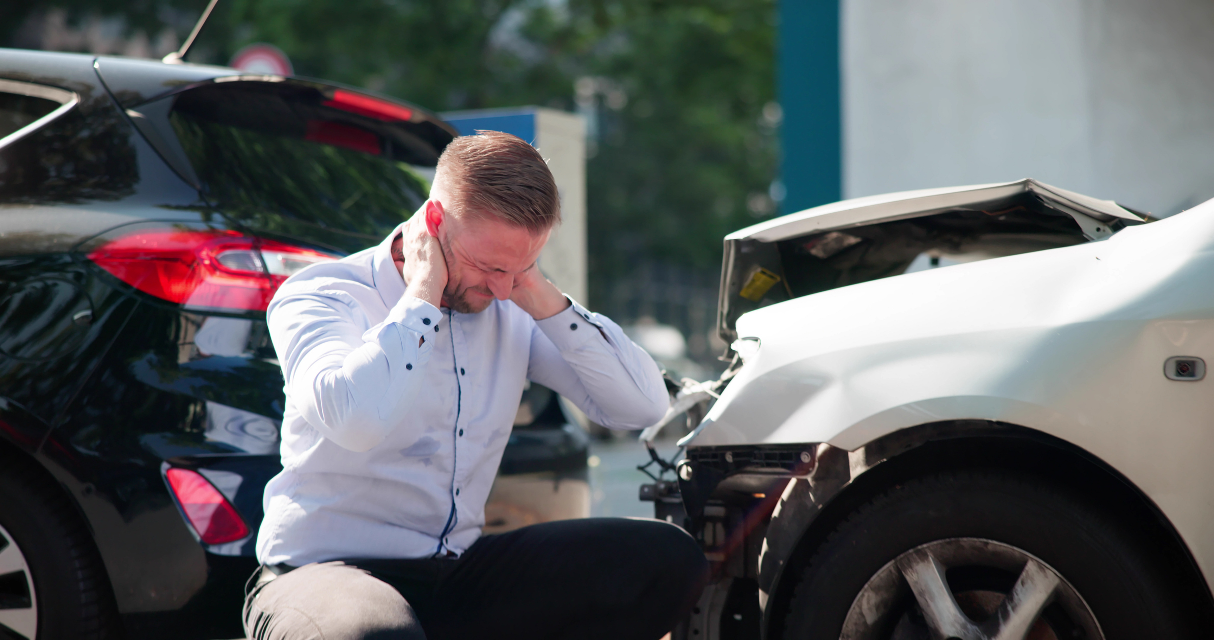 Driver holding his neck beside two damaged cars after a collision