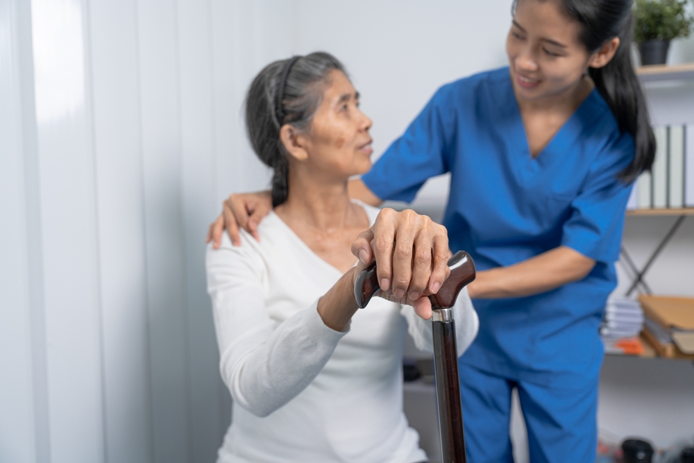 A nurse assisting an older woman who is holding a cane during therapy
