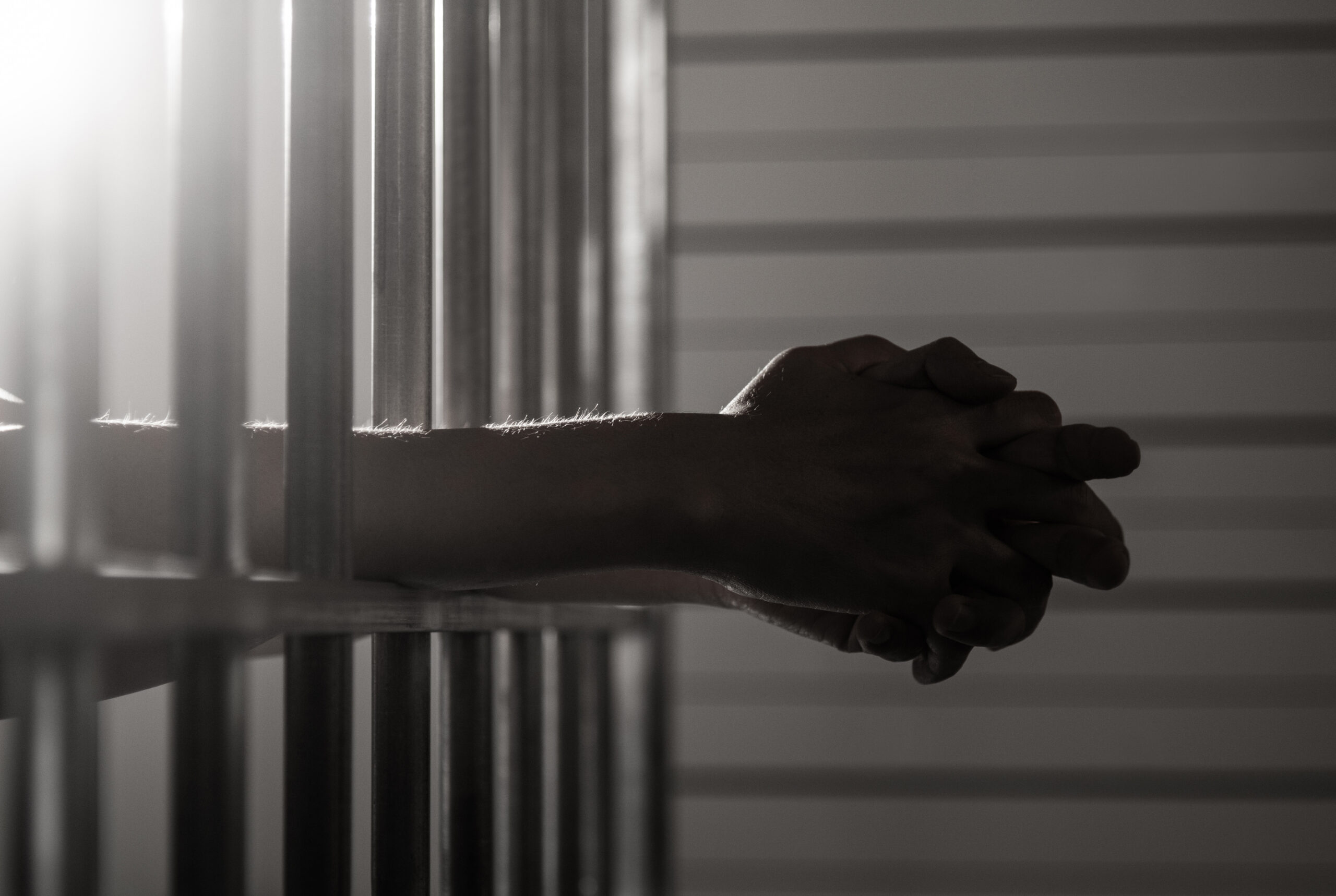 Hands clasped behind jail bars, illustrating the stakes of an assault or battery charge