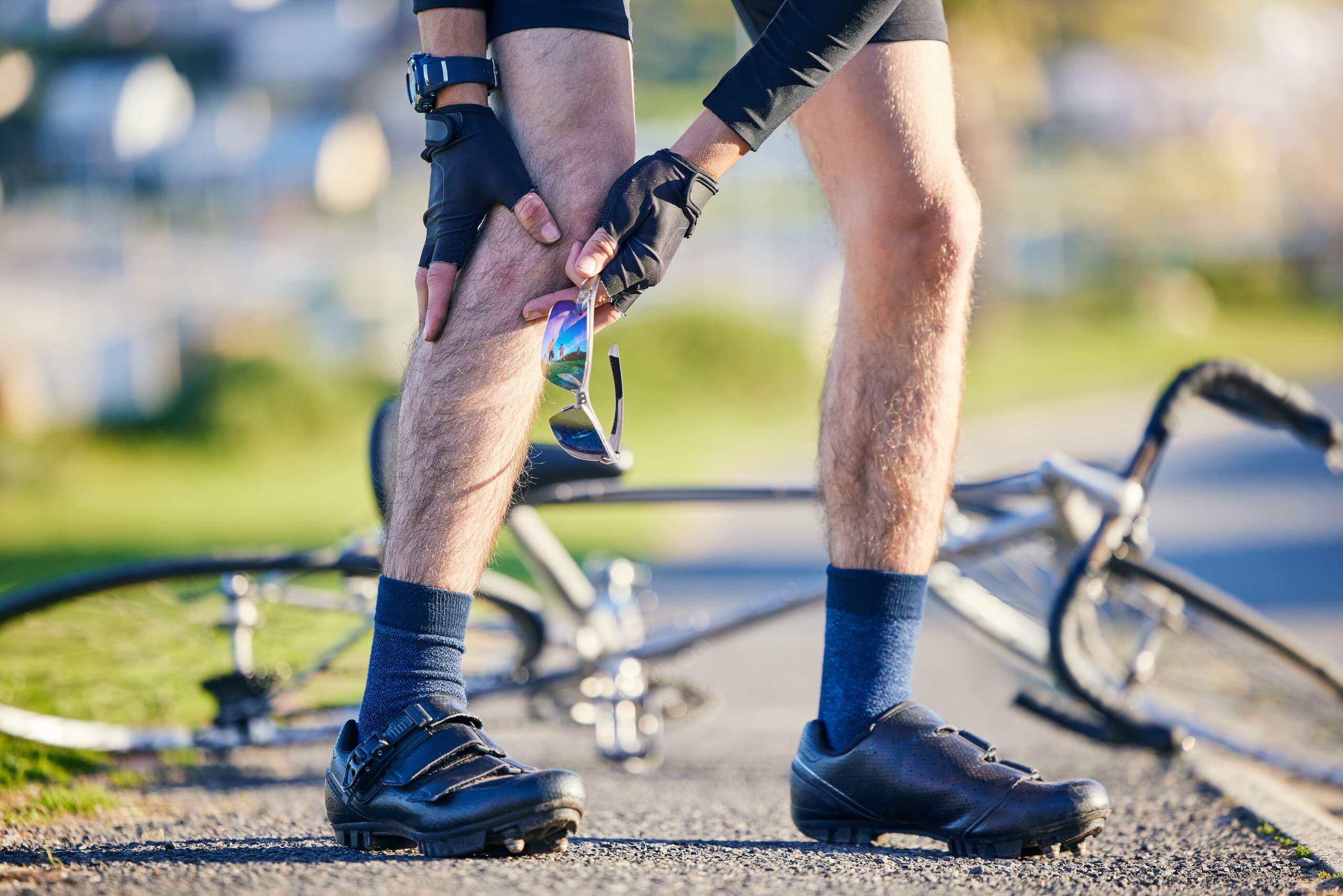 A cyclist holding their knee beside a fallen bicycle.