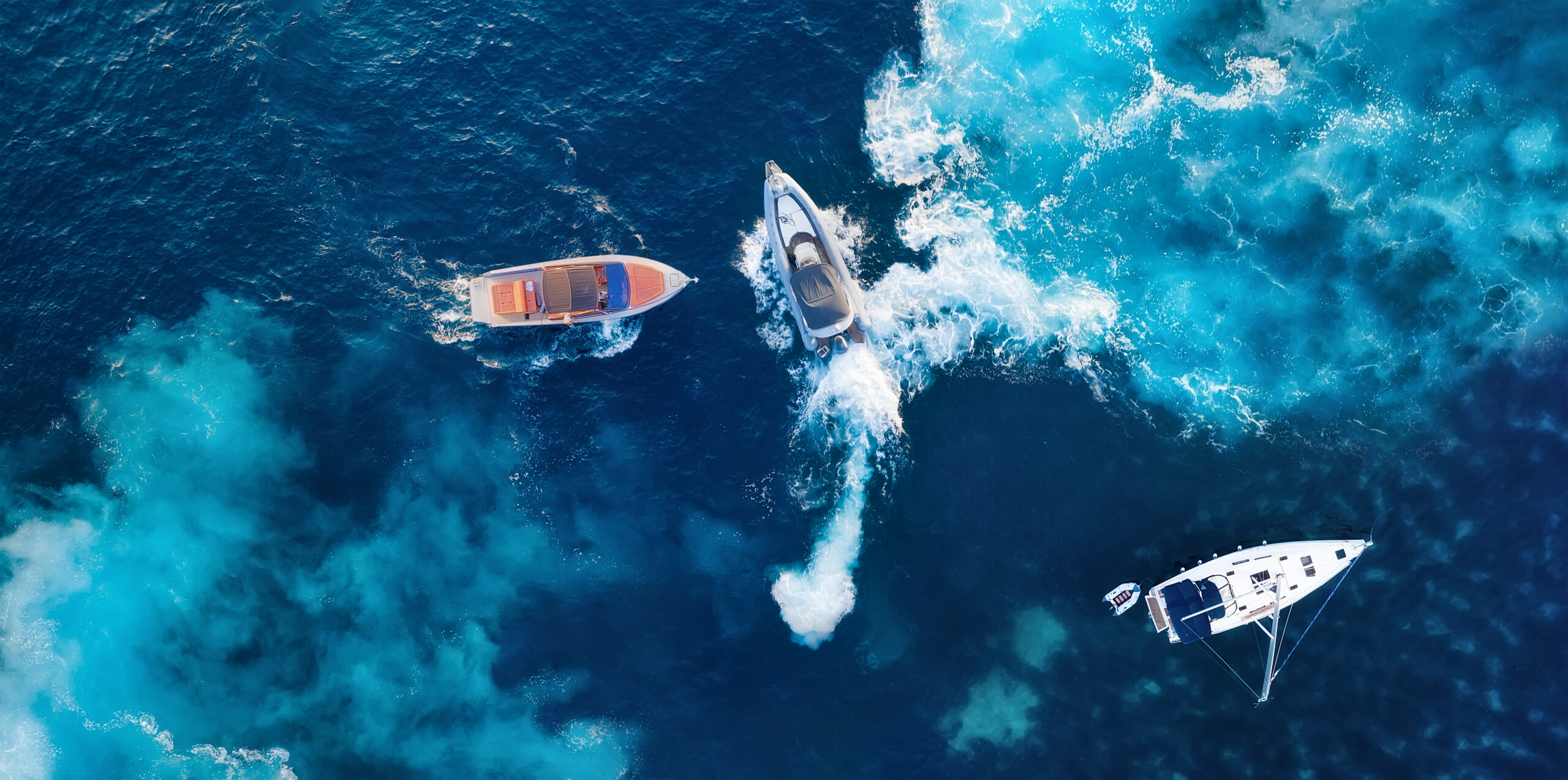 Aerial view of three boats on blue water, with a motorboat moving through foamy wake